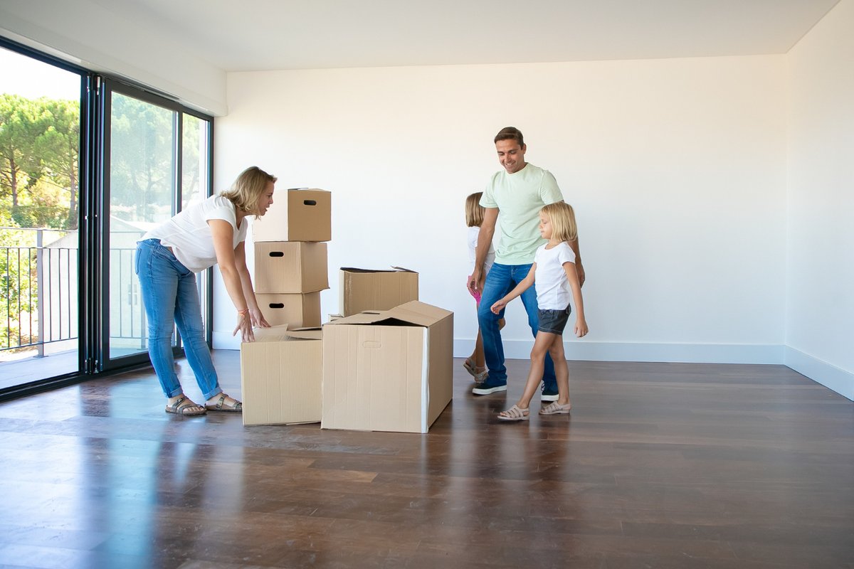Happy parents and daughters opening boxes and unpacking things in their new empty flat