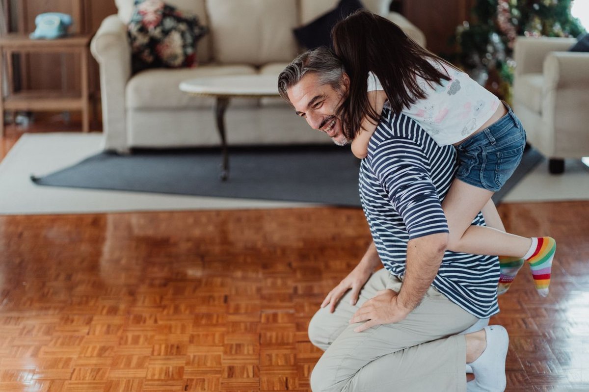 A joyful father and daughter play indoors, highlighting their affectionate bond in a cozy setting.