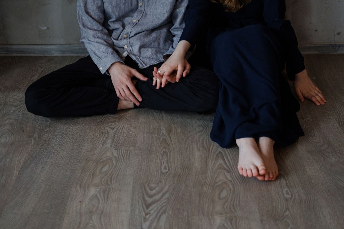 A couple holds hands while sitting on a wooden floor, showcasing a tender moment.