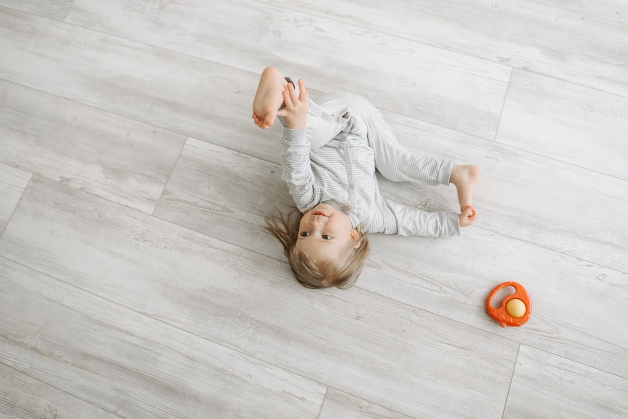Cute child lying and playing with a toy on wooden floor, dressed warmly in pajamas.