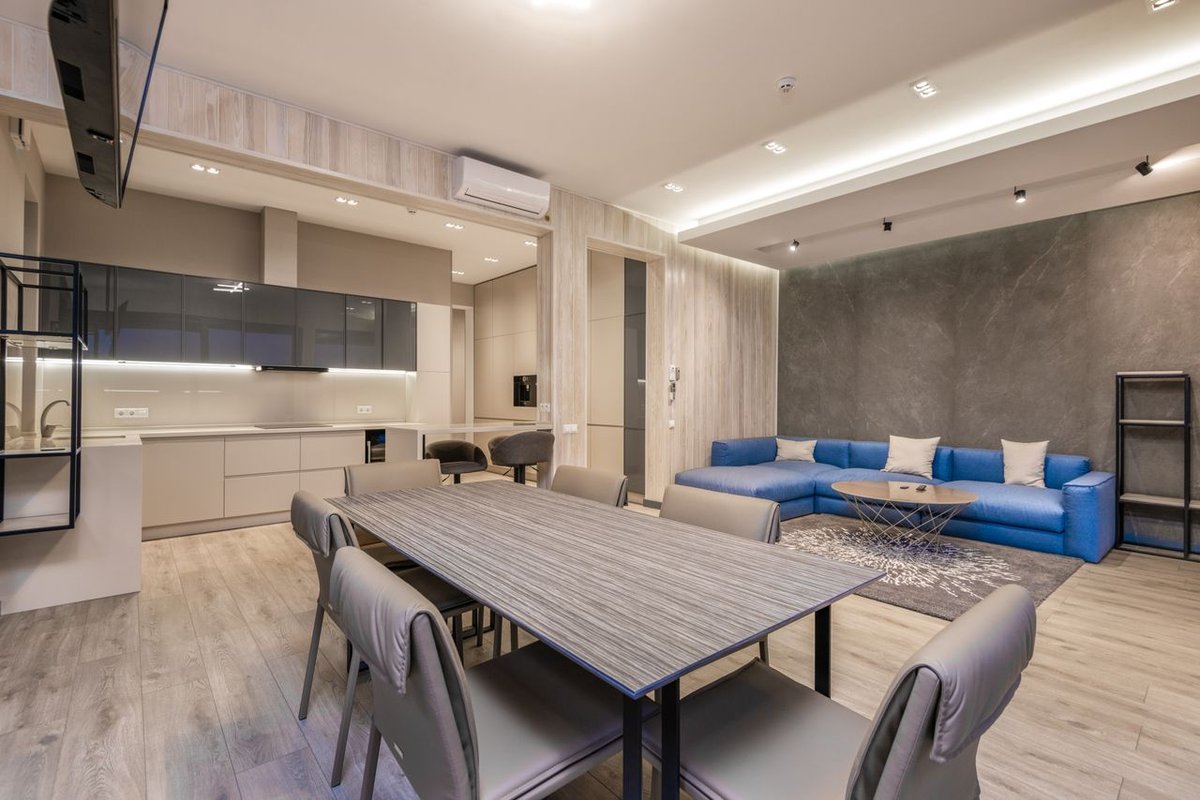 Sleek modern living room with dining area and kitchen, featuring a blue sofa and elegant decor.