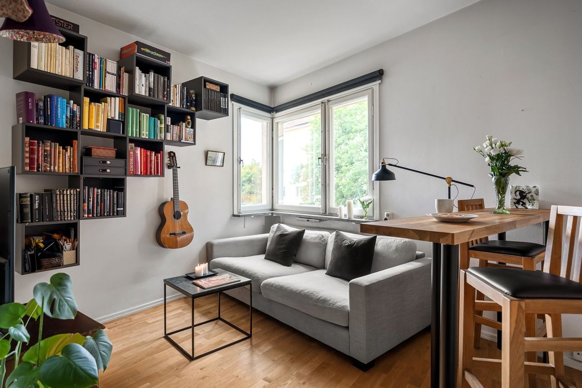 Inviting living room interior with bookshelves, guitar, and grey couch under natural light