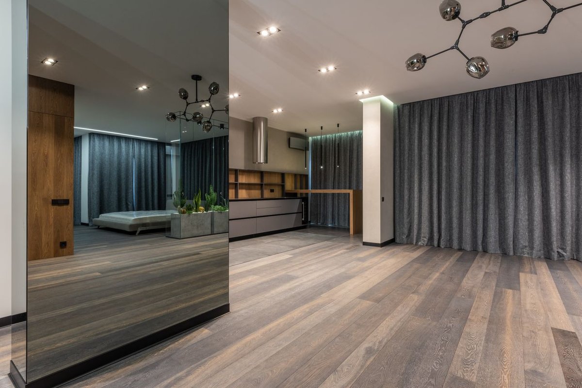 Spacious modern interior with wooden flooring, mirror wall, and contemporary decor for a sleek and elegant look.