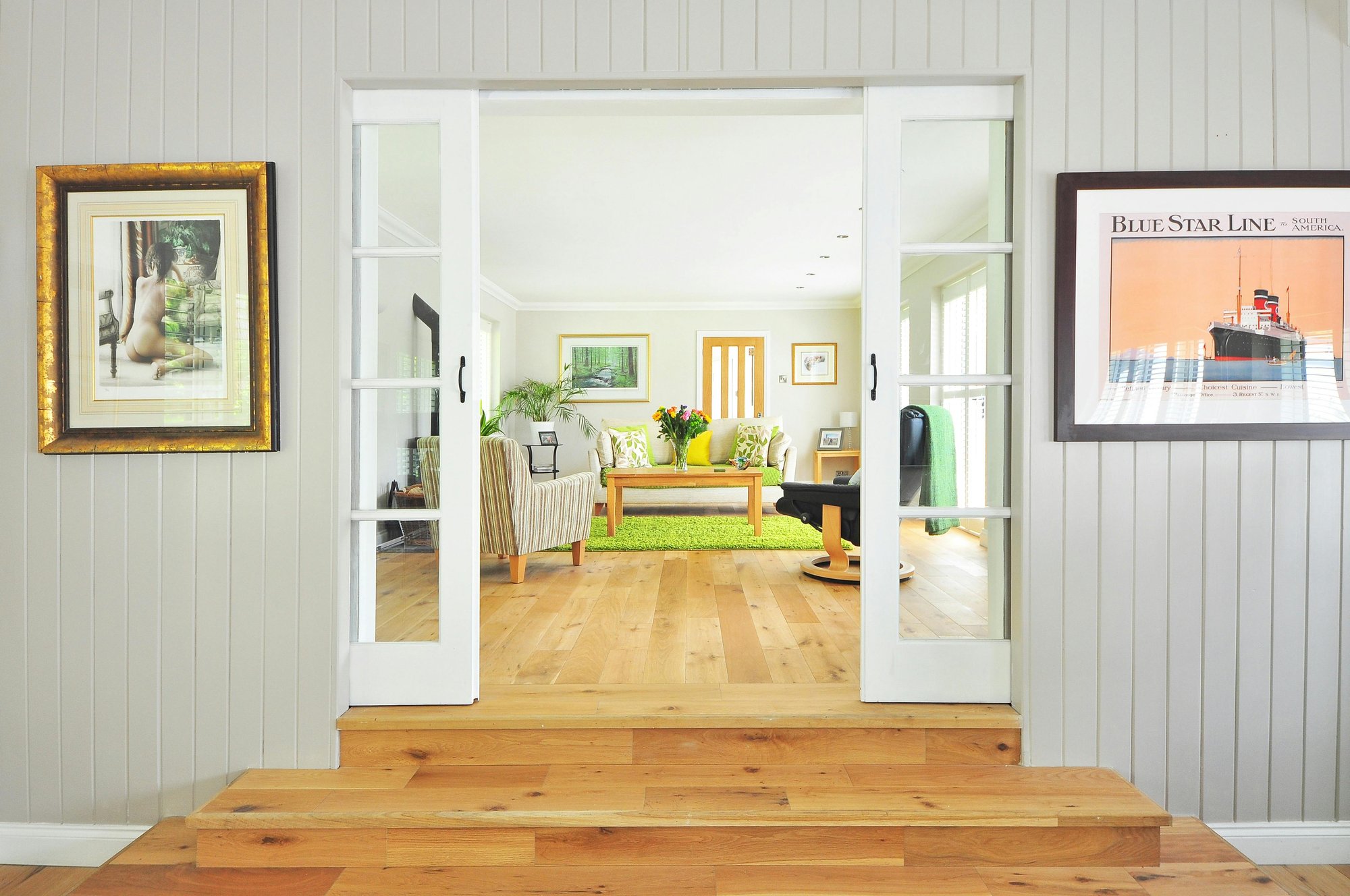 View through white double doors into cozy living room with green rug on wood flooring, striped armchair, and natural light.
