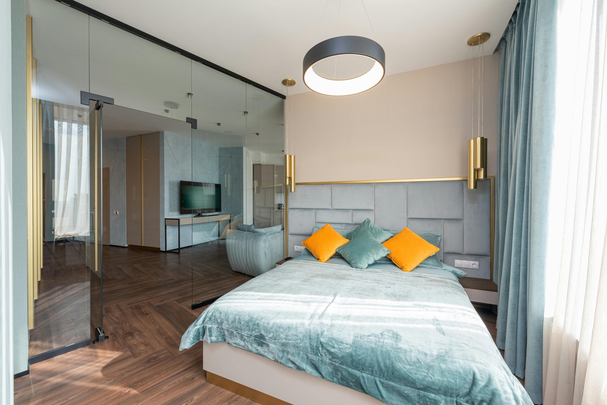 Modern bedroom with teal bedding, dark wood flooring, pendant lights, and floor-to-ceiling windows with sheer curtains.