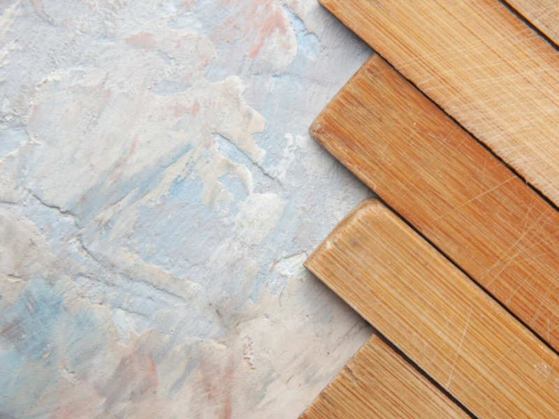 Diagonal light wood planks overlap beside a marbled wall with blue, white, and pink hues—organic meets artistic texture.
