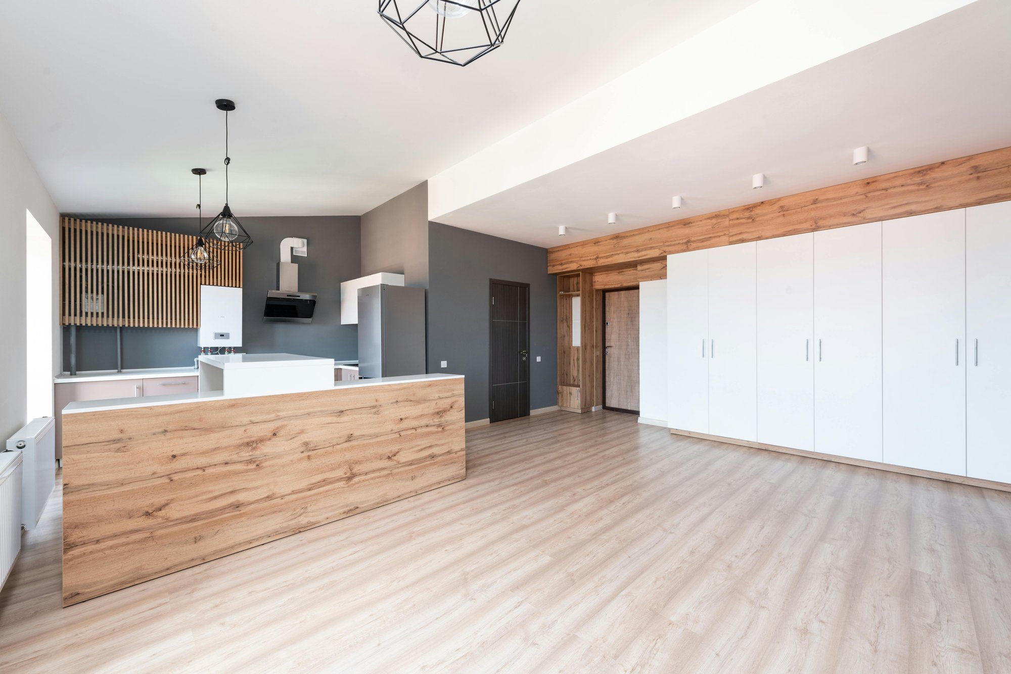 Modern open-plan space with laminated wood flooring, pendant lights, skylight, white cabinets, and wood-accented kitchen.
