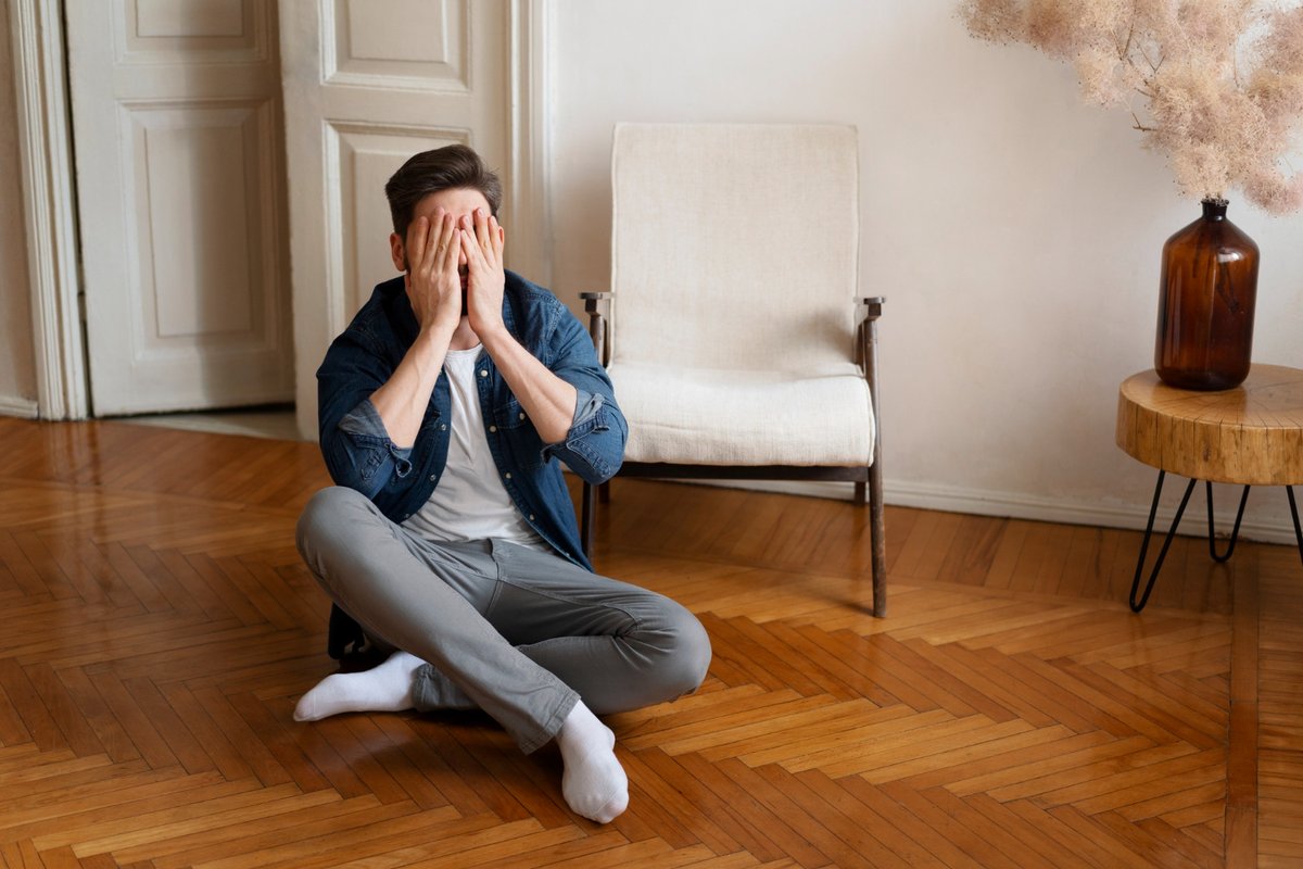 Full shot man covering his face while sitting on the floor