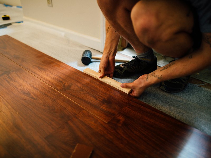 Person installing dark hardwood flooring with mallet and block, transitioning from carpet in a home renovation project.